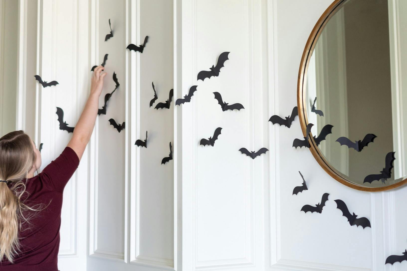 A woman attaching black paper bats to a wall inside a home