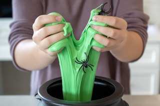 A person pulling green slime filled with plastic spiders out of a black plastic cauldron.