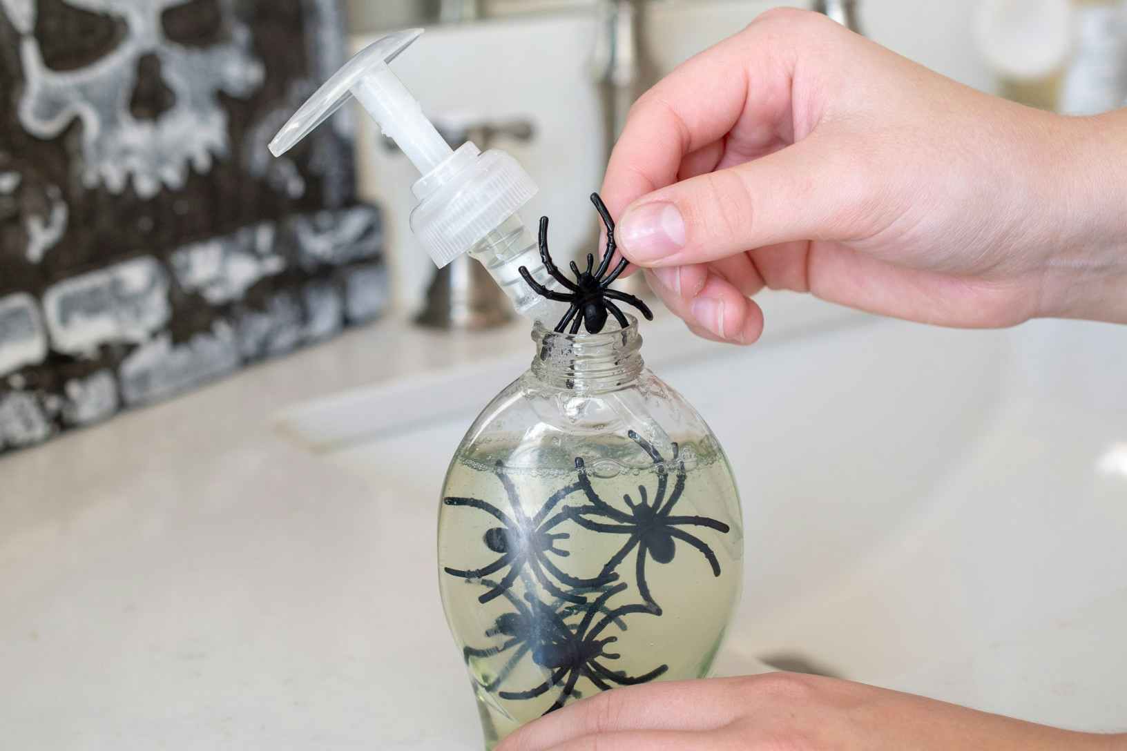 A person adding plastic spiders to a clear bottle of hand soap.