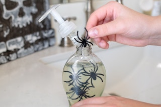 A person adding plastic spiders to a clear bottle of hand soap.