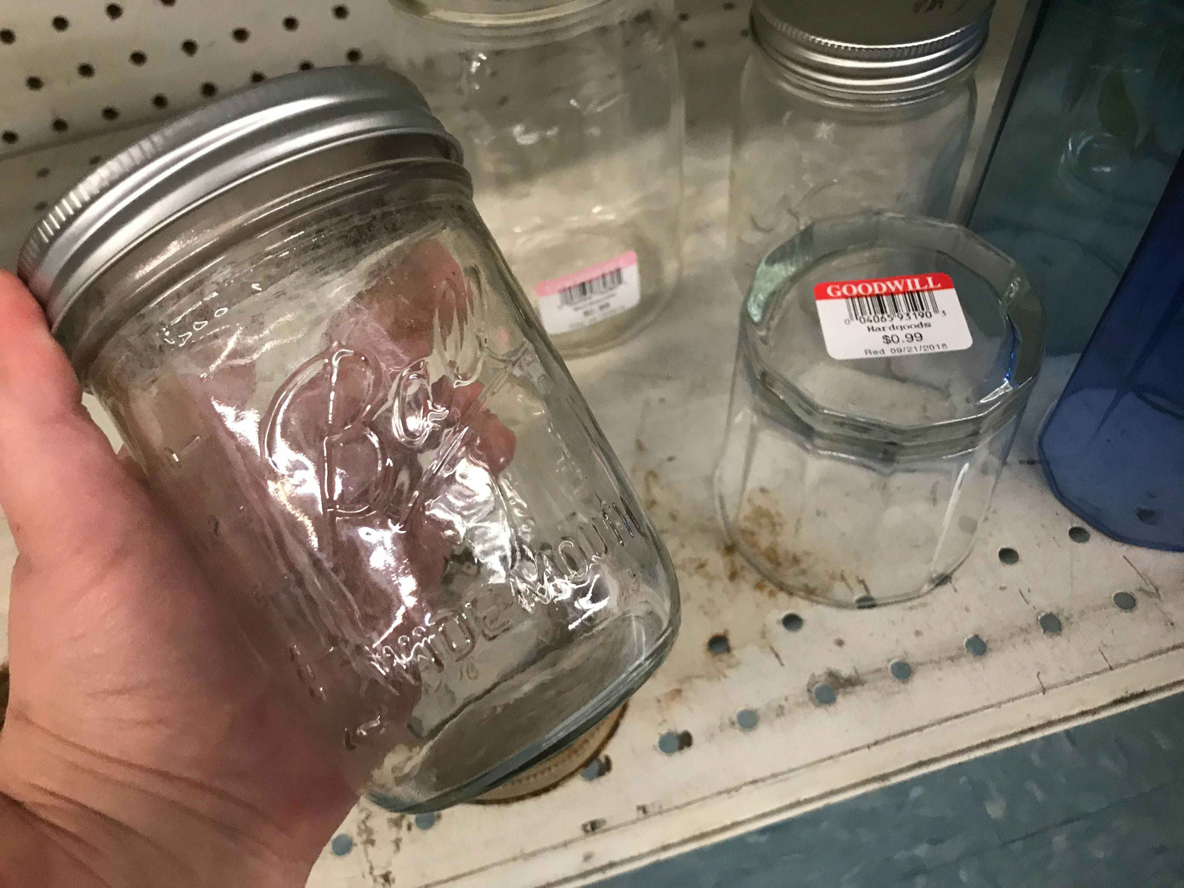 A person holding an empty canning jar in front of a shelf at Goodwill.