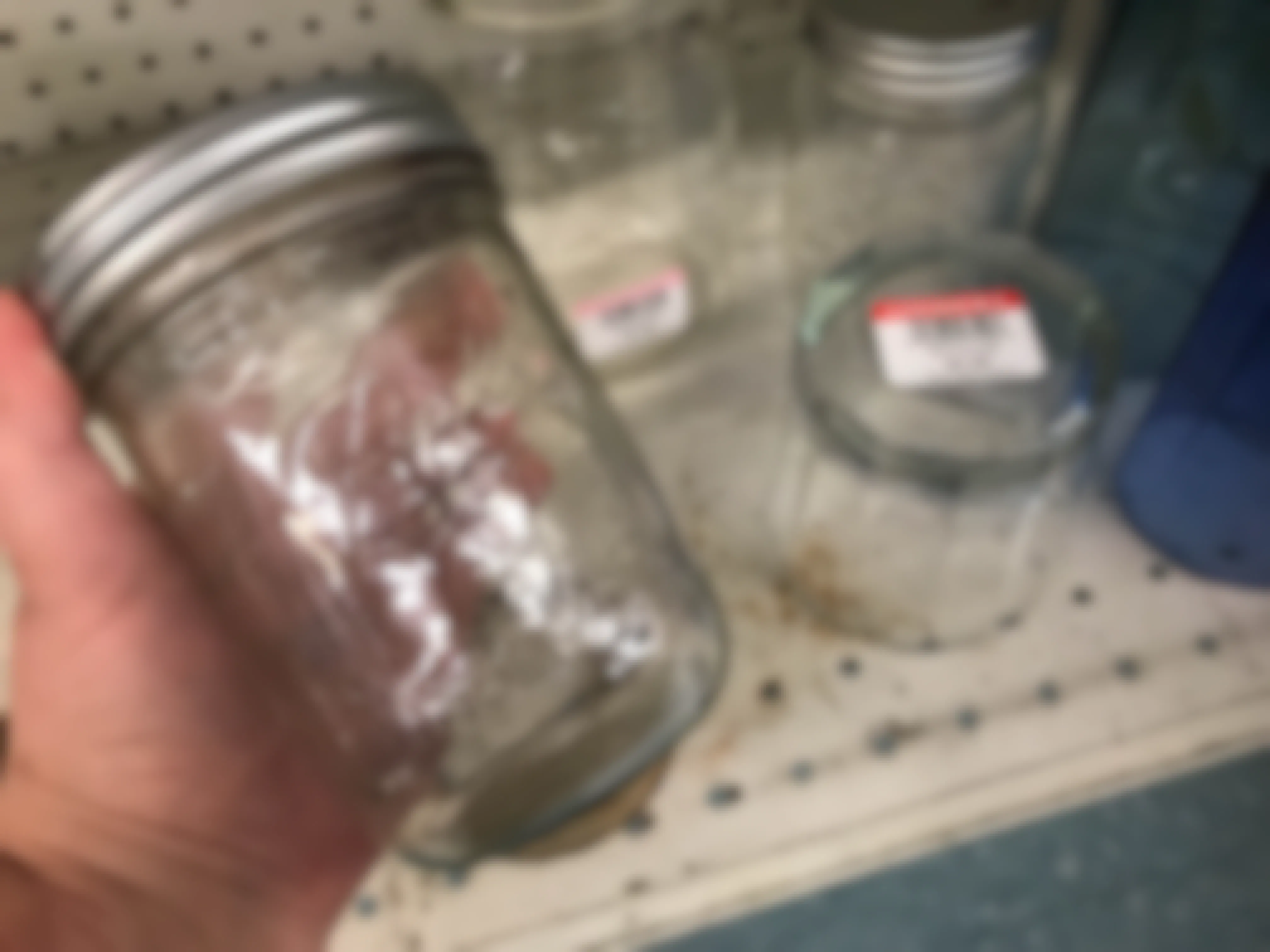 A person holding an empty canning jar in front of a shelf at Goodwill.