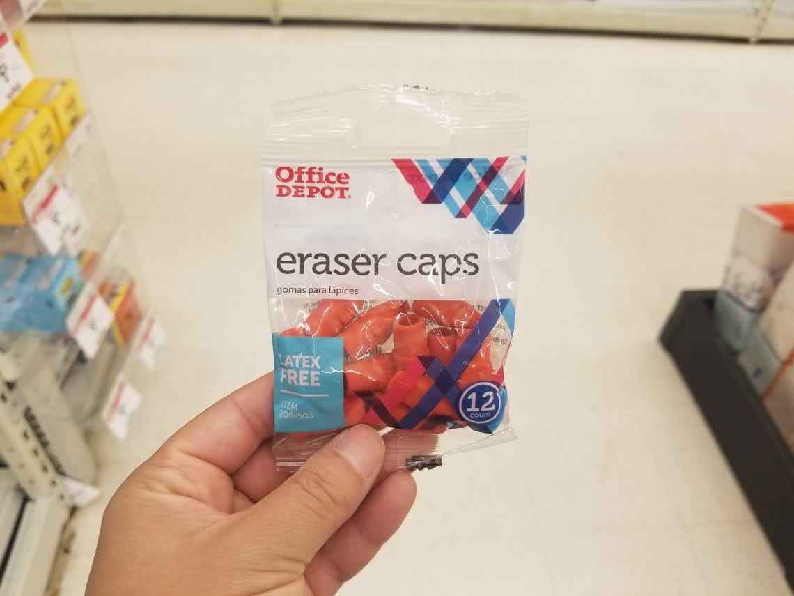 A person's hand holding up a package of Office Depot eraser caps in an aisle at Office Depot.