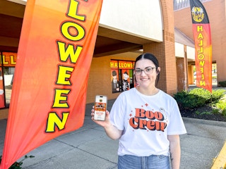 a person standing outside of spirit halloween holding up a phone and smiling