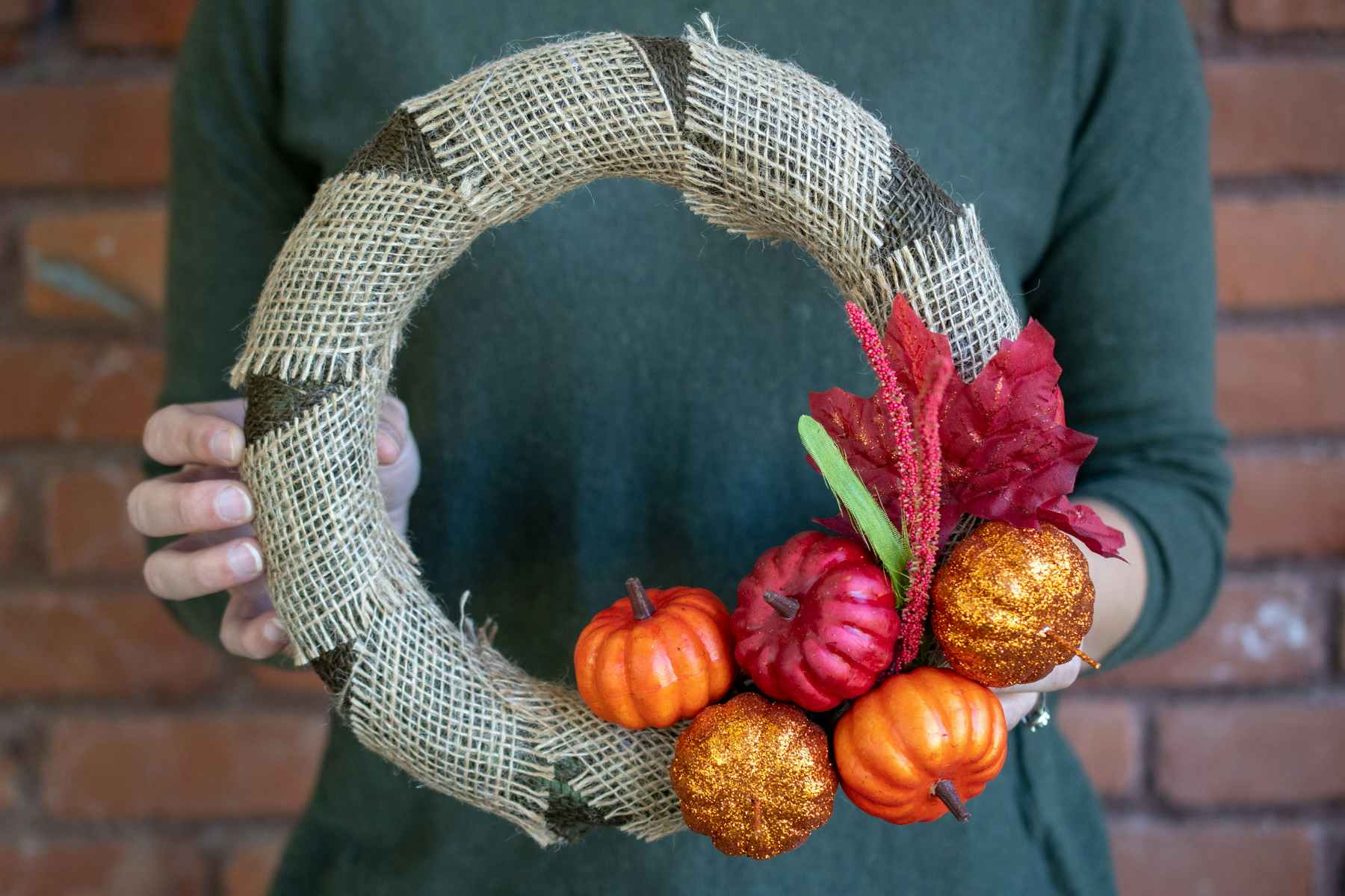 A fall wreath wrapped with burlap, adorned with pumpkins and fall leaves.