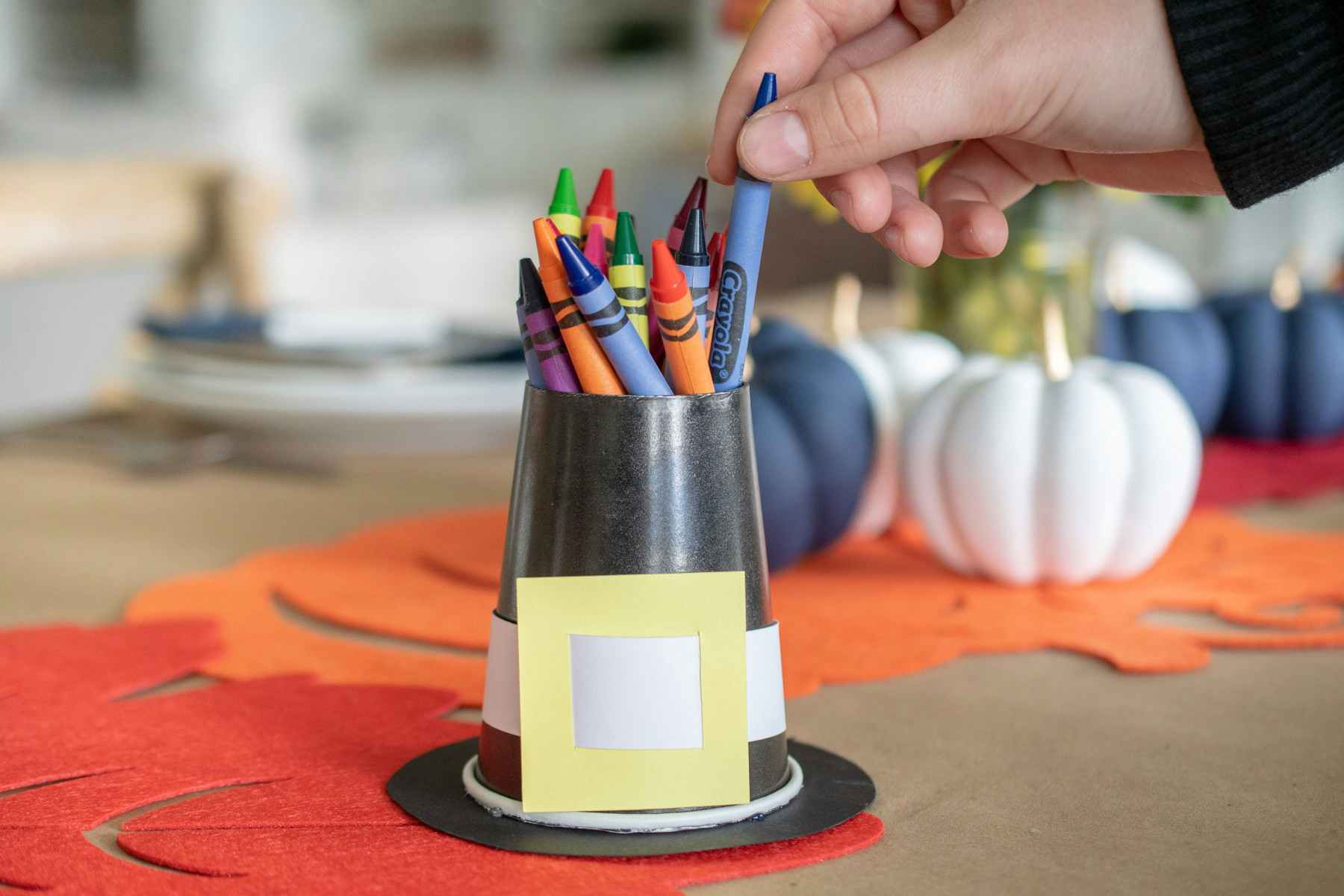A person pulling a crayon out of a cup that looks like a pilgrims hat.