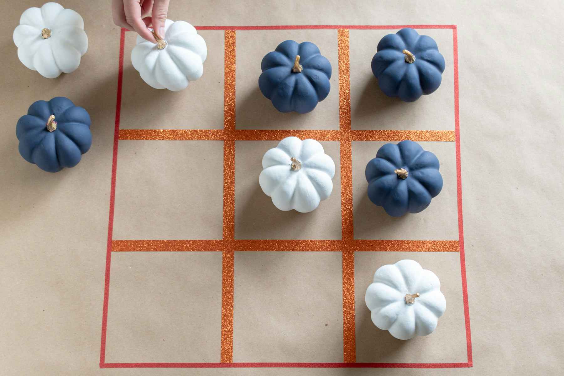 A person play tic-tac-toe with painted pumpkins and a board made from washi tape.