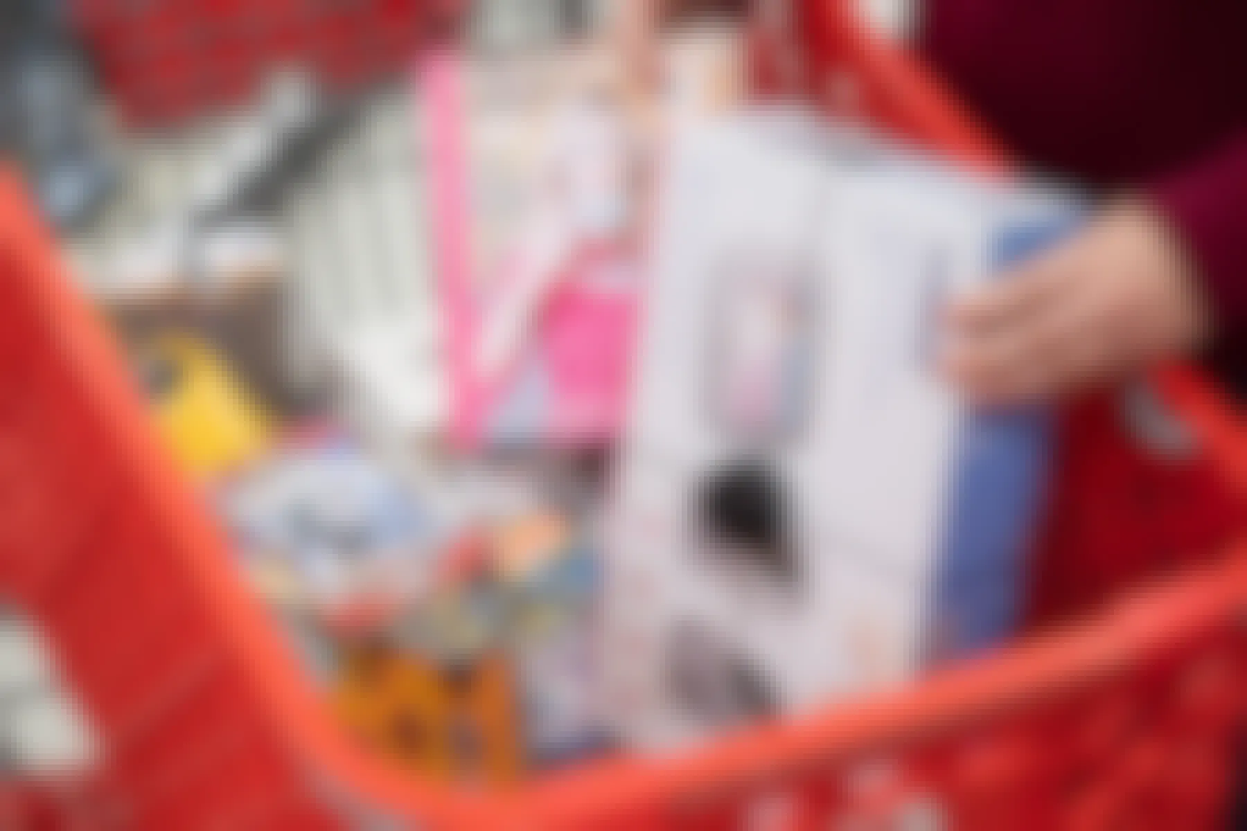 A person's hands placing a Vtech baby monitor and a book into a Target shopping cart filled with other items.