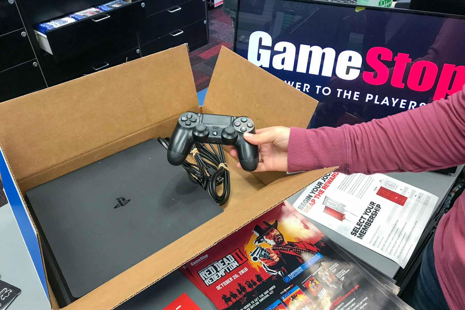 A person holding open a ps4 box sitting on a GameStop counter.