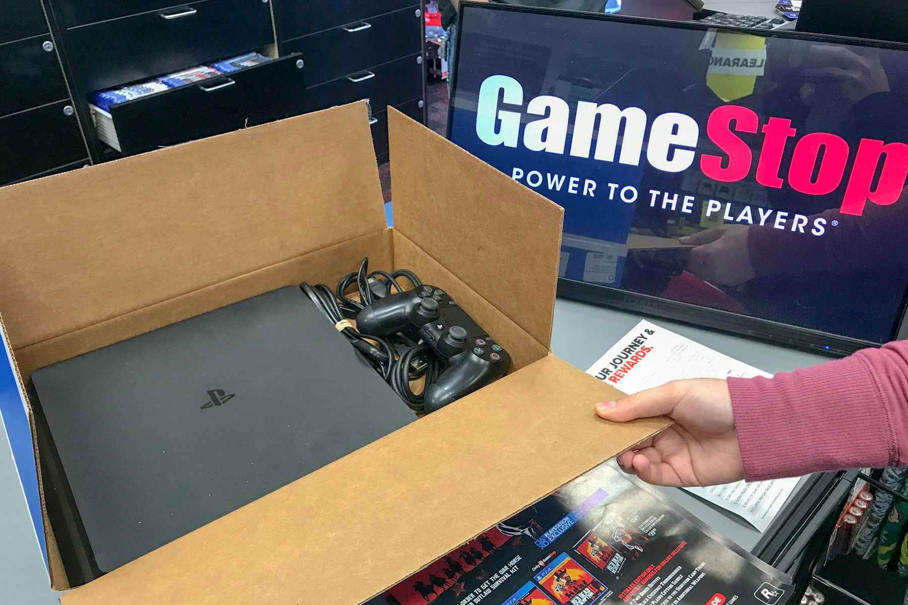 A person holding open a ps4 box sitting on a GameStop counter.