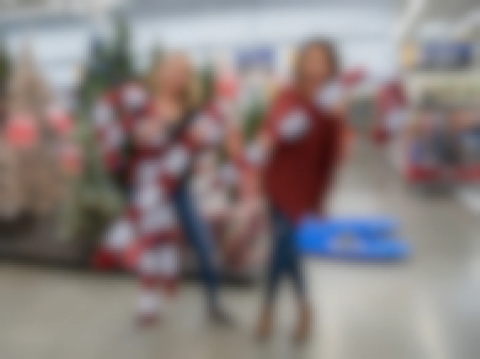 two women hold giant candy canes in front of the Christmas tree section in Walmart.