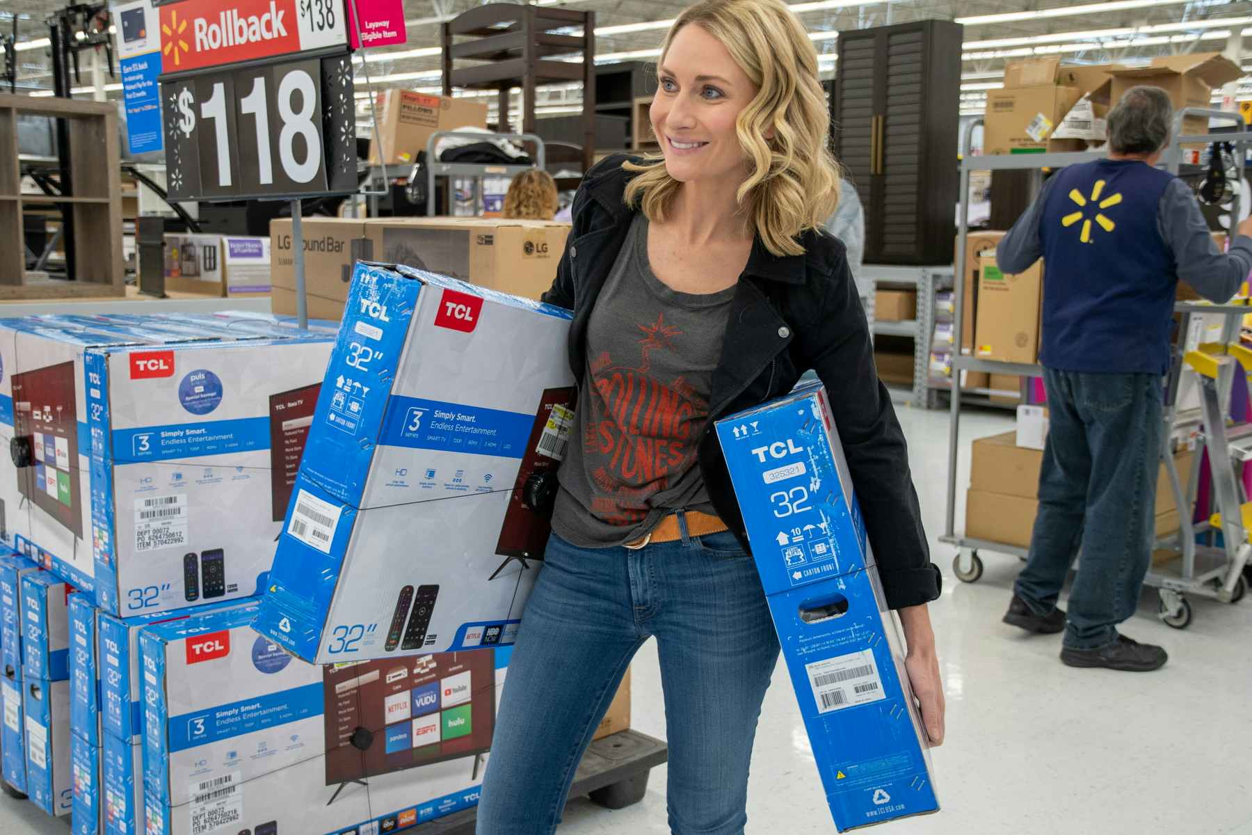 A woman with two tvs in her hand, stands in front of a display of TV's inside Walmart.