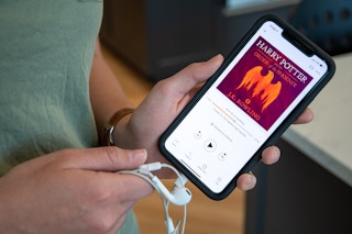 A woman holding an iPhone and head phones with Harry Potter and the Order of the Phoenix from audible on the screen.
