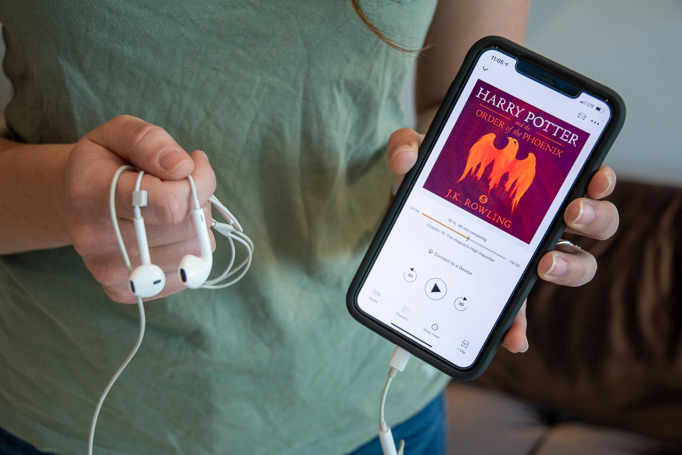 A woman holding an iPhone and head phones with Harry Potter and the Order of the Phoenix from audible on the screen.