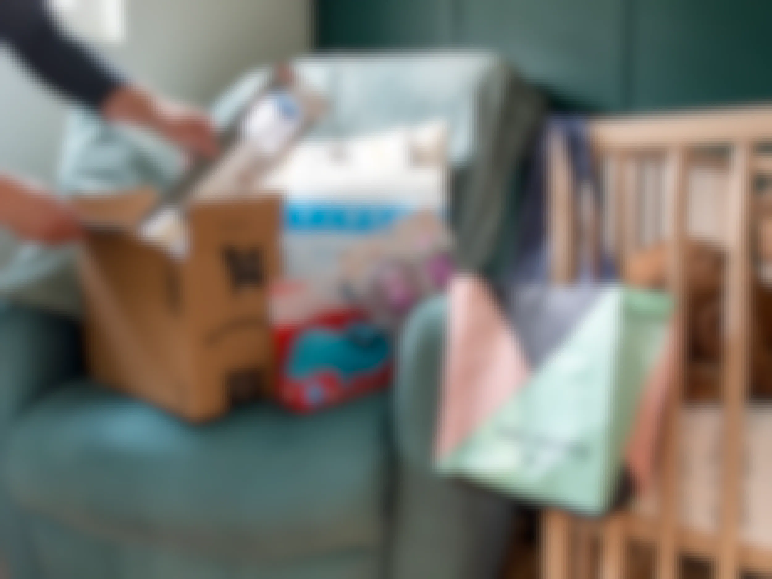 A person pulling baby products out of an amazon box. An amazon welcome bag is hanging on a crib near by
