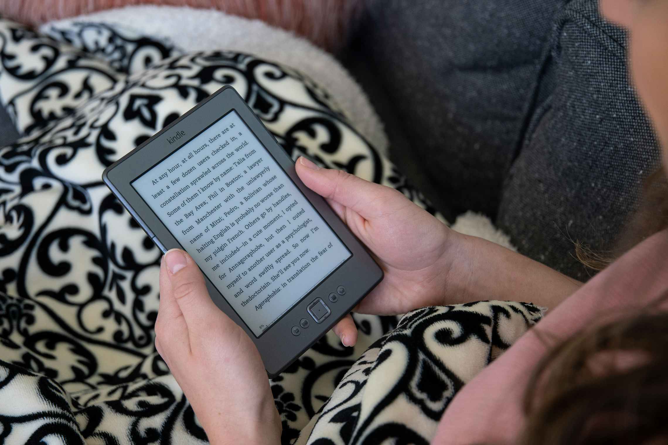 A woman holding an Amazon Kindle with a book displayed on the screen.