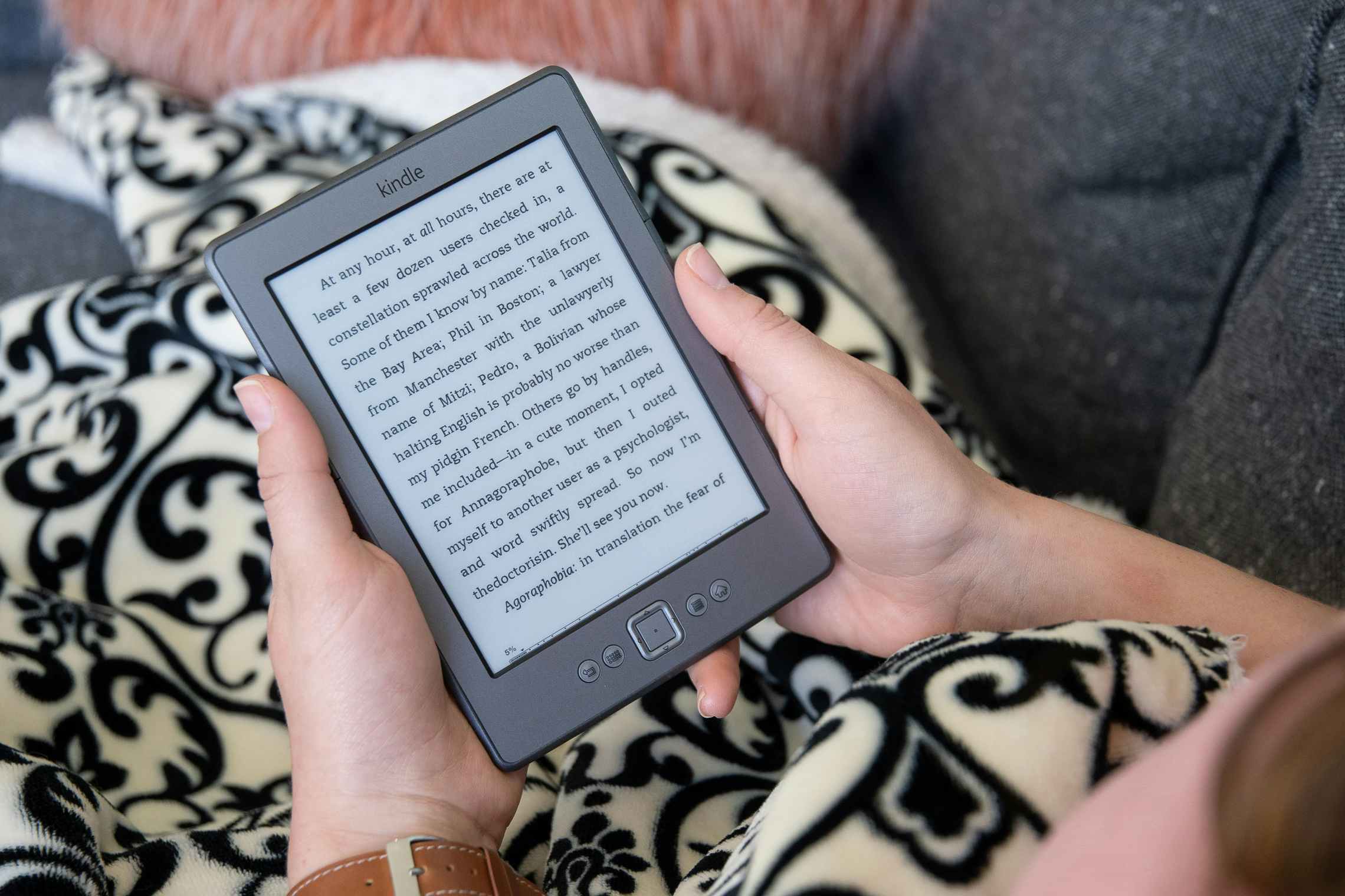 A woman holding an Amazon Kindle with a book displayed on the screen.