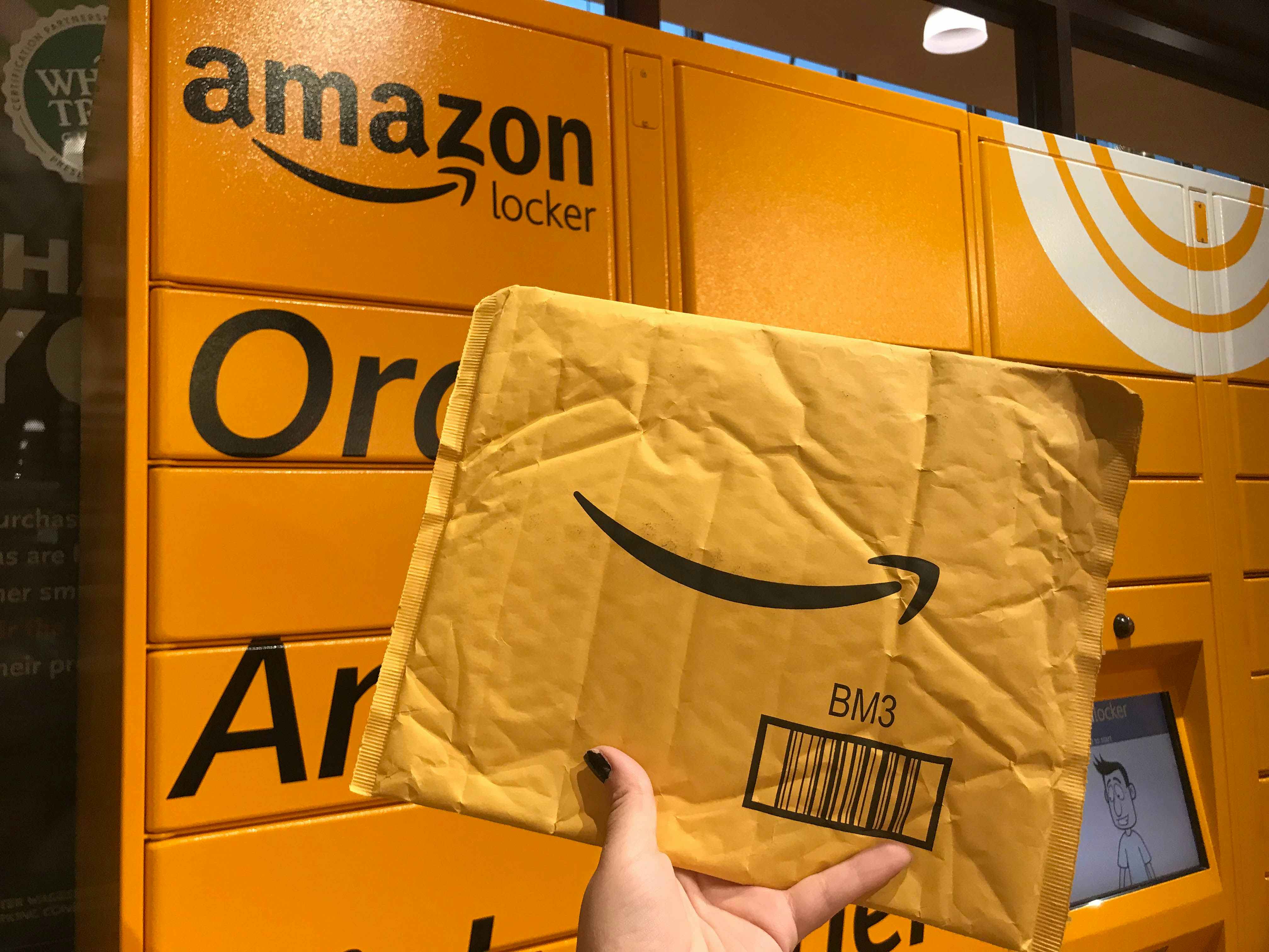A person holding up an Amazon package in front of an Amazon locker