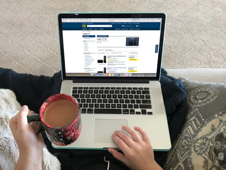 A person holding a mug of coffee and browsing through the Apple TV products on Best Buy's website.