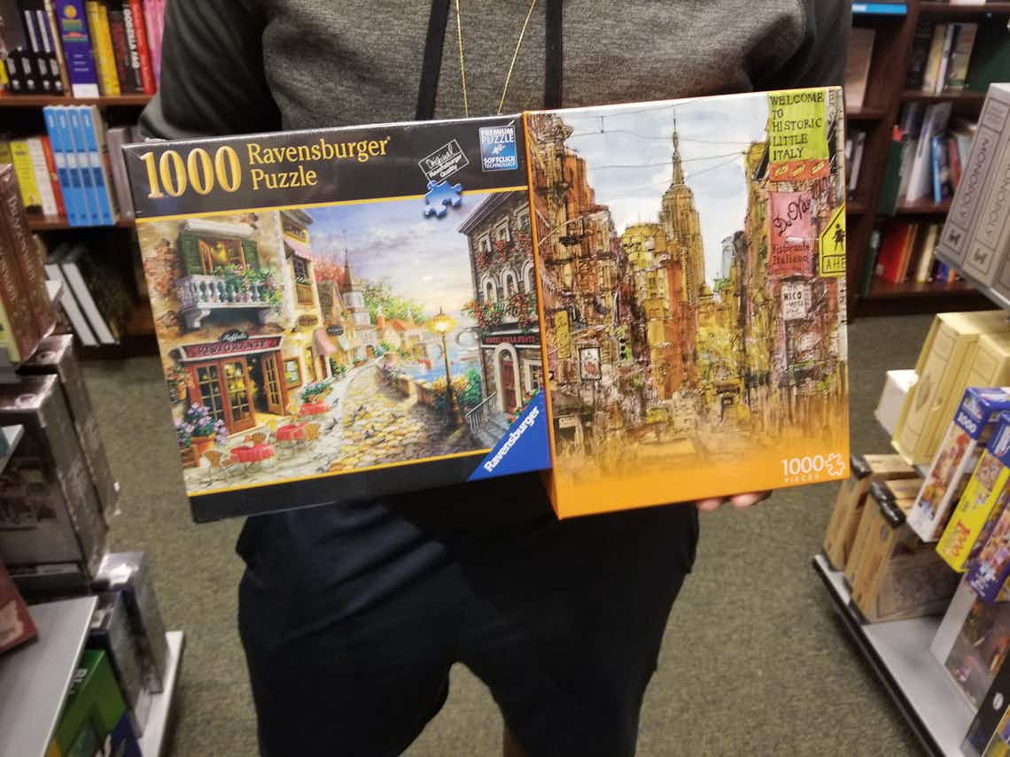 Two 1000 piece puzzles held by a person in a book store.