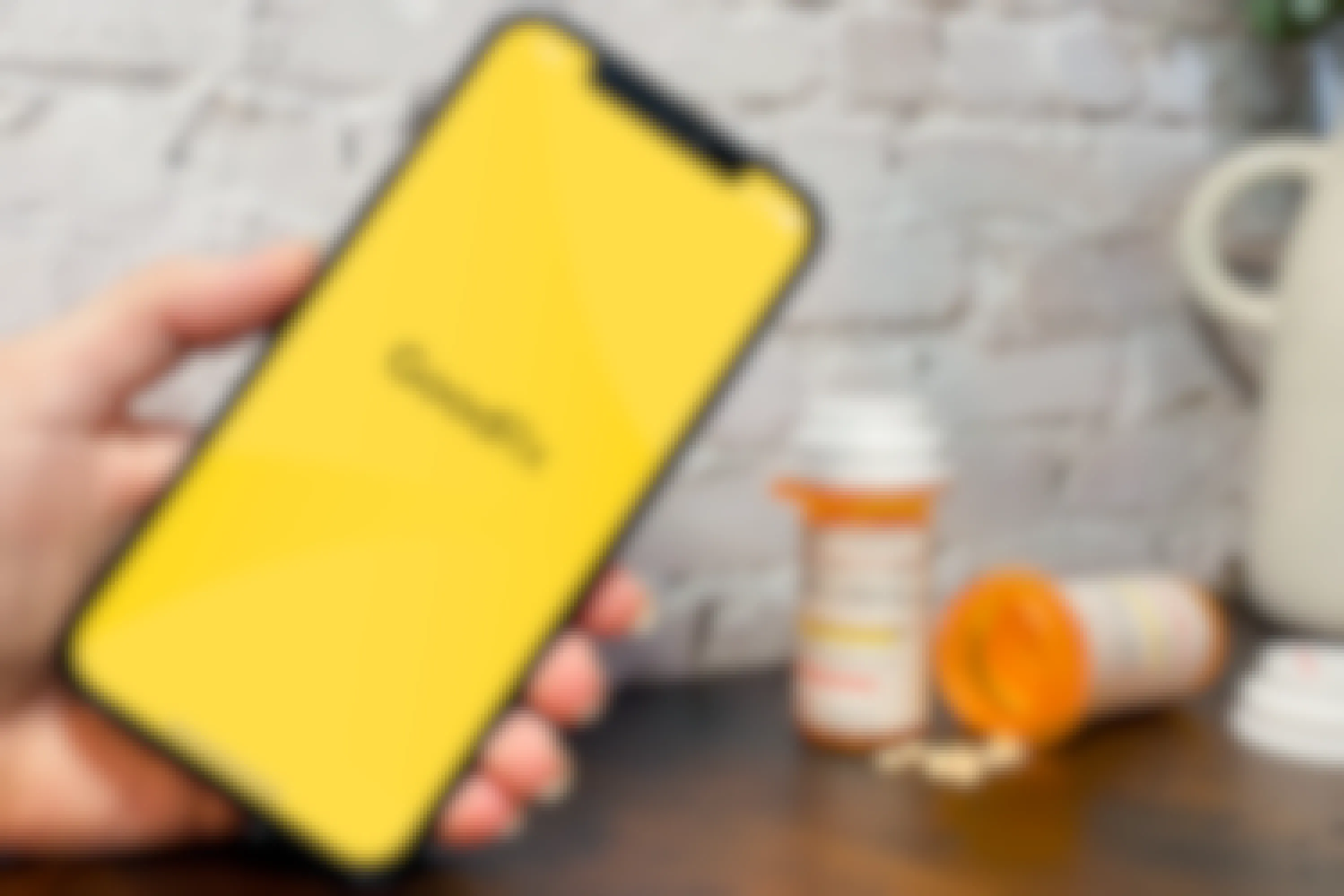 Someone holding up a phone displaying the GoodRX app launch screen with some prescription medication on a table in the background