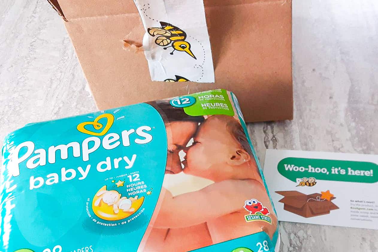 A package of Pampers diapers on a table next to a shipping box from BzzAgent and a card that reads, "woo-hoo, it's here!