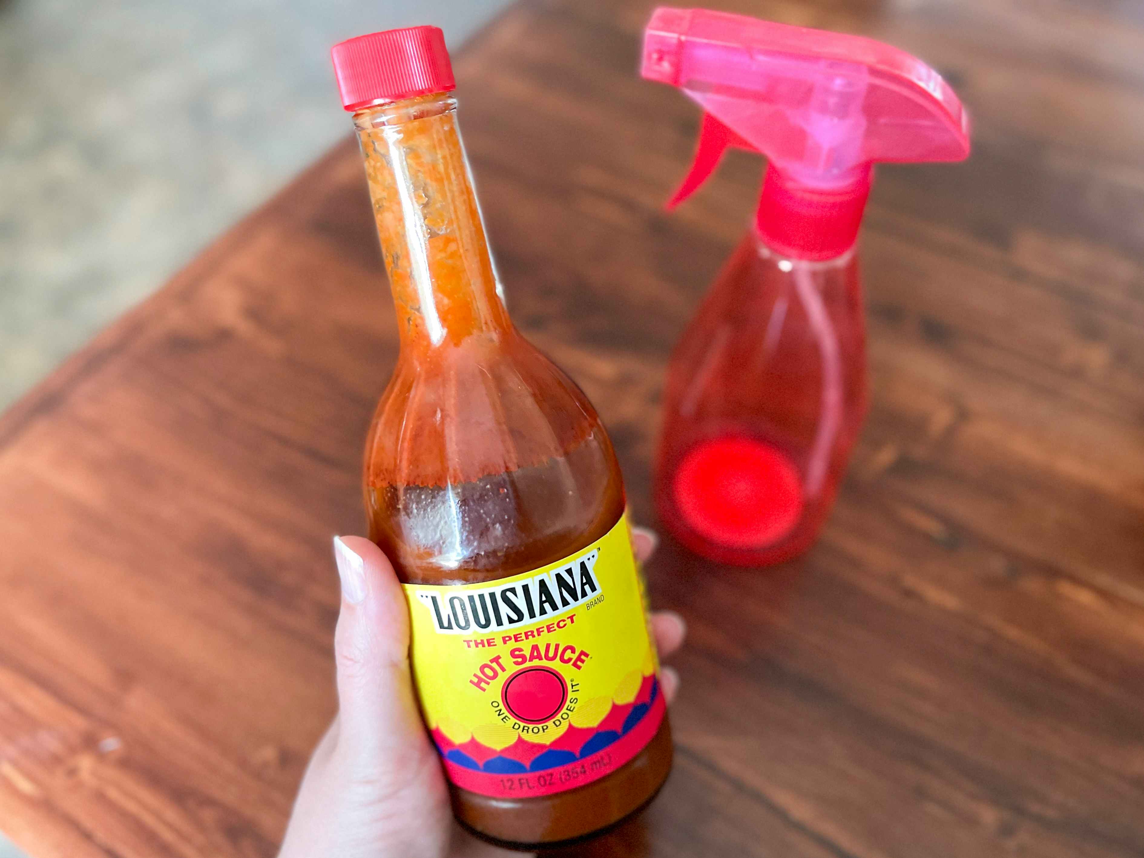 A bottle of hot sauce held next to a red spray bottle sitting on a table.