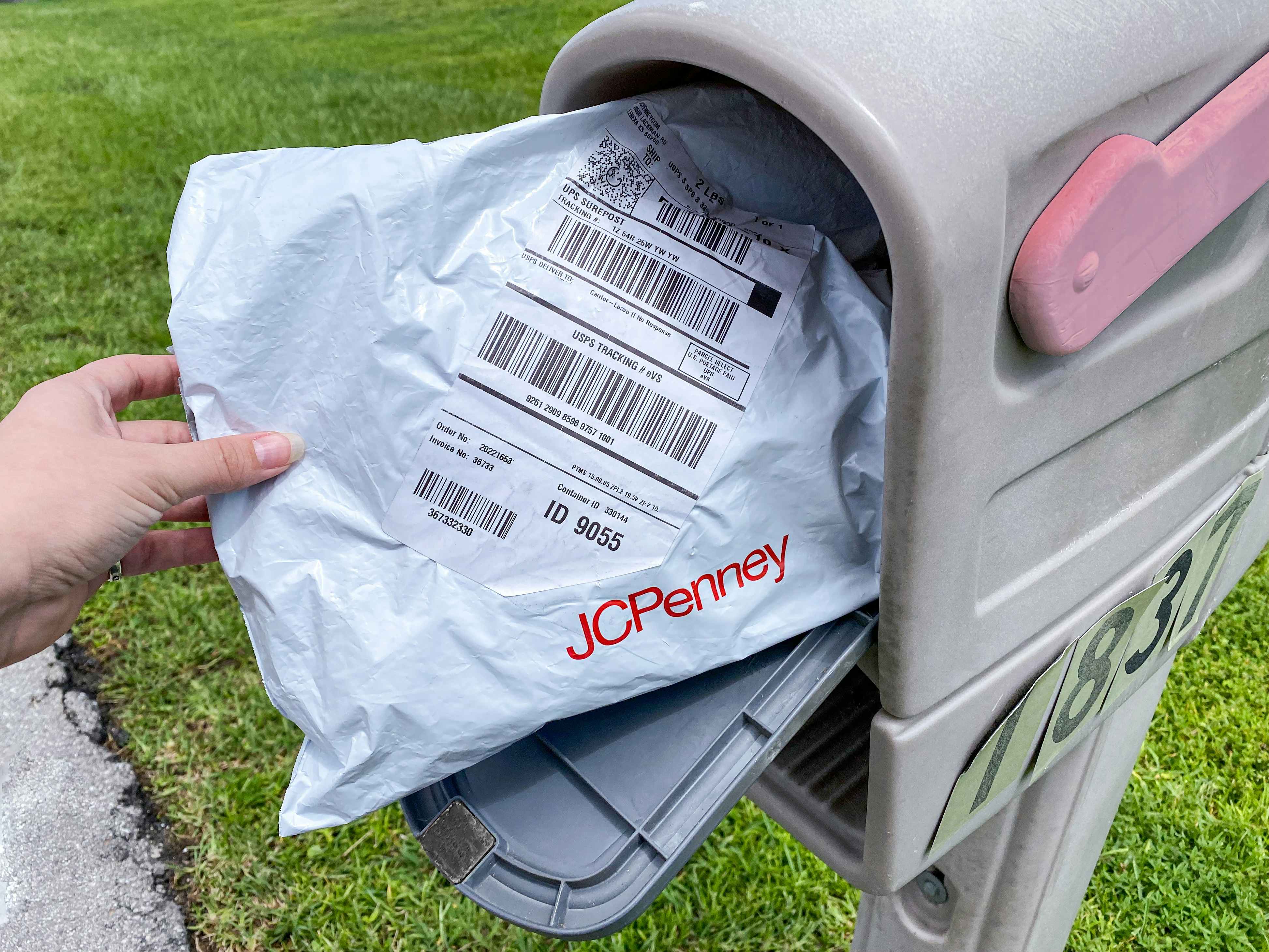A person's hand taking a JCPenney package out of a mailbox.