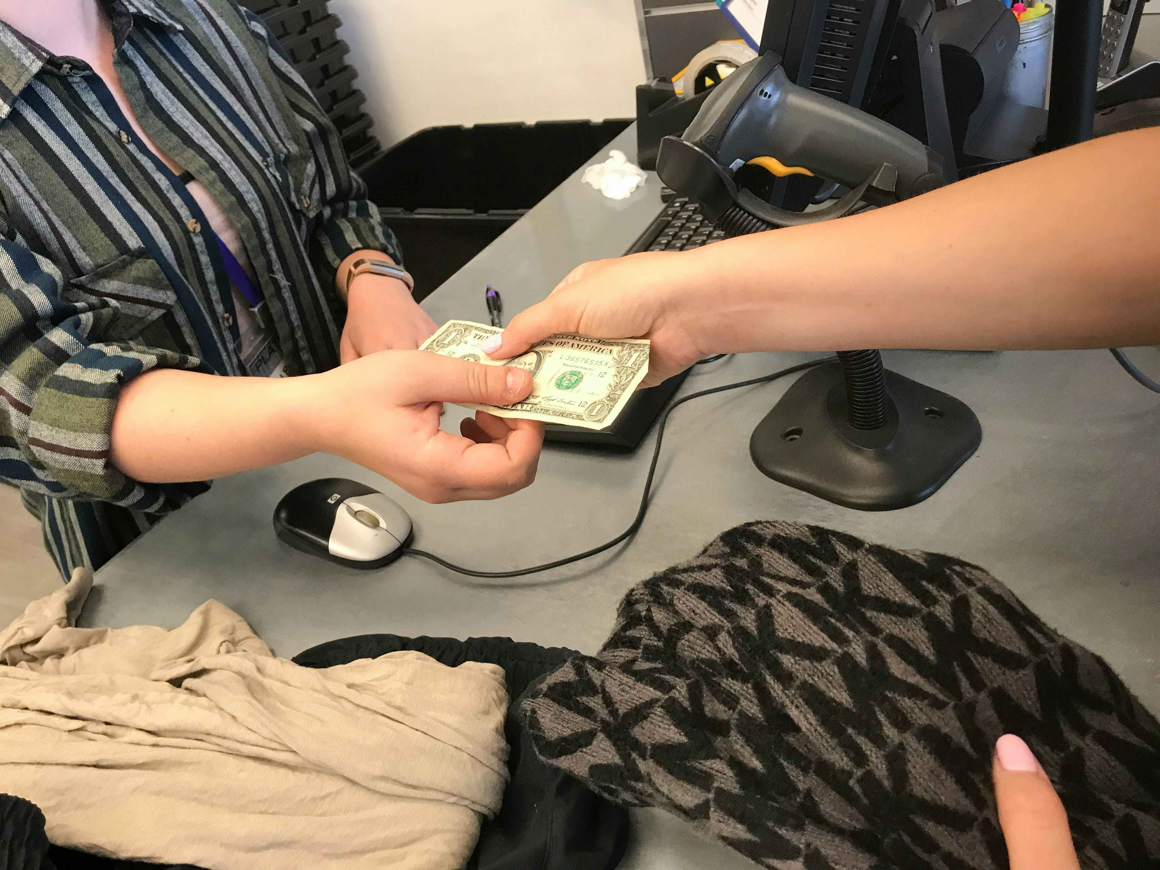 A person receiving a dollar bill from a store employee at a register.