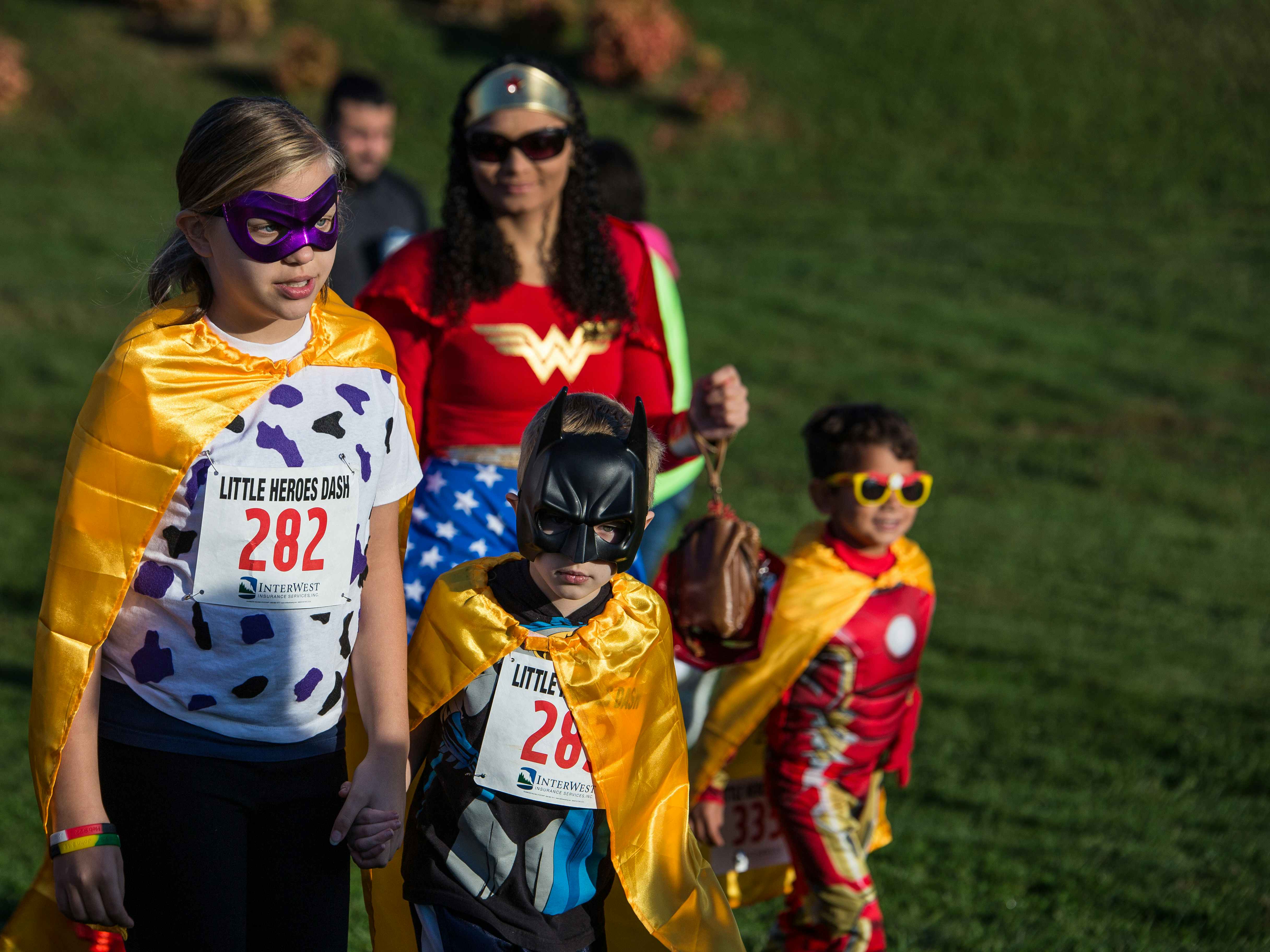 Children and their mother dressed as superheroes with fun run numbers attached to their chest.