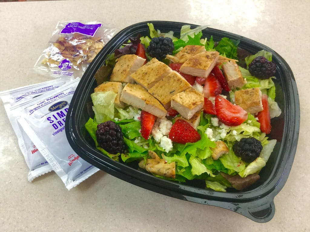 A Wendy's chicken salad in a container sitting on a table next to packets of dressing and nuts.