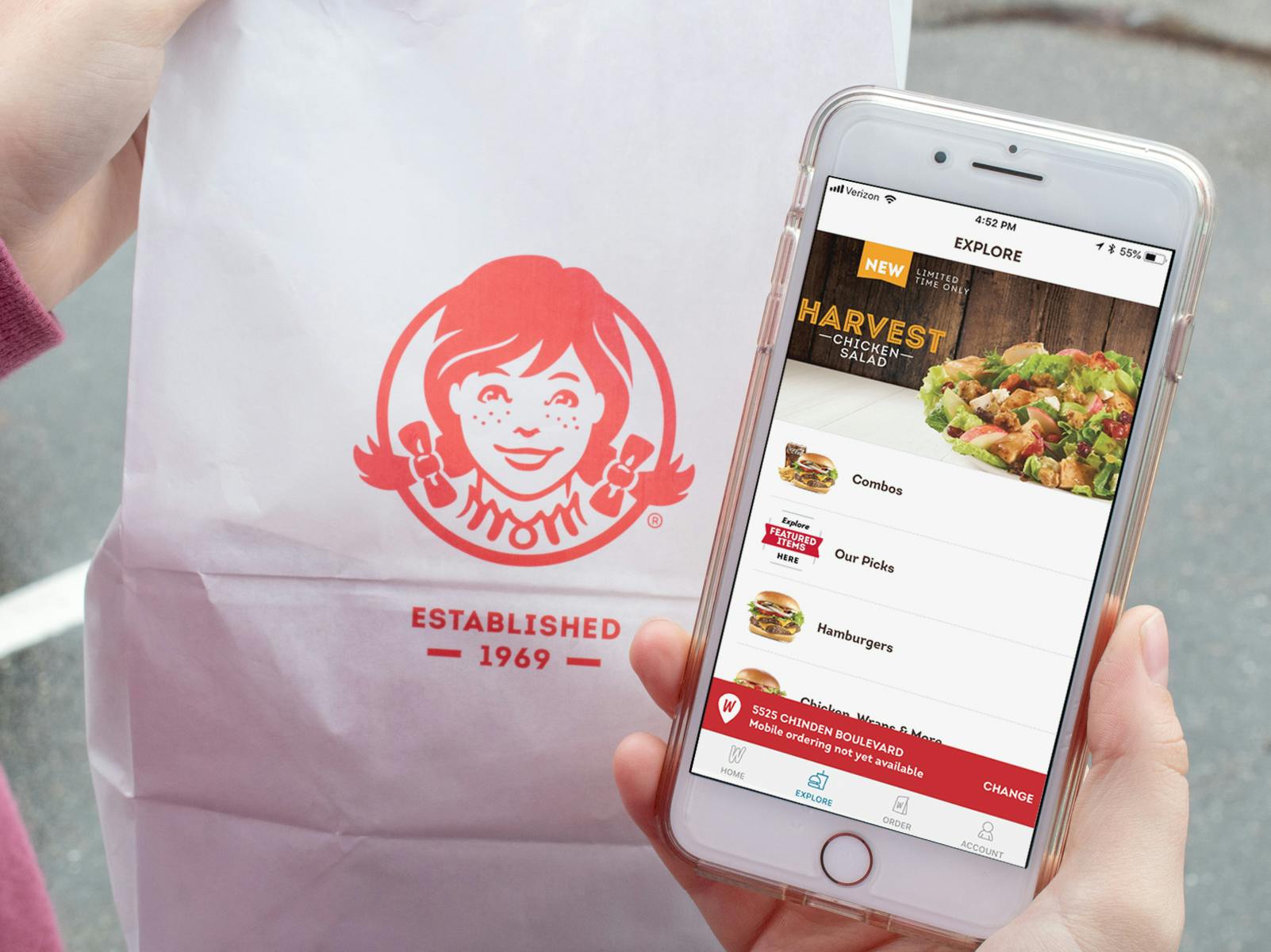 Someone holding a Wendy's takeout bag next to an iPhone displaying the Wendy's mobile app.