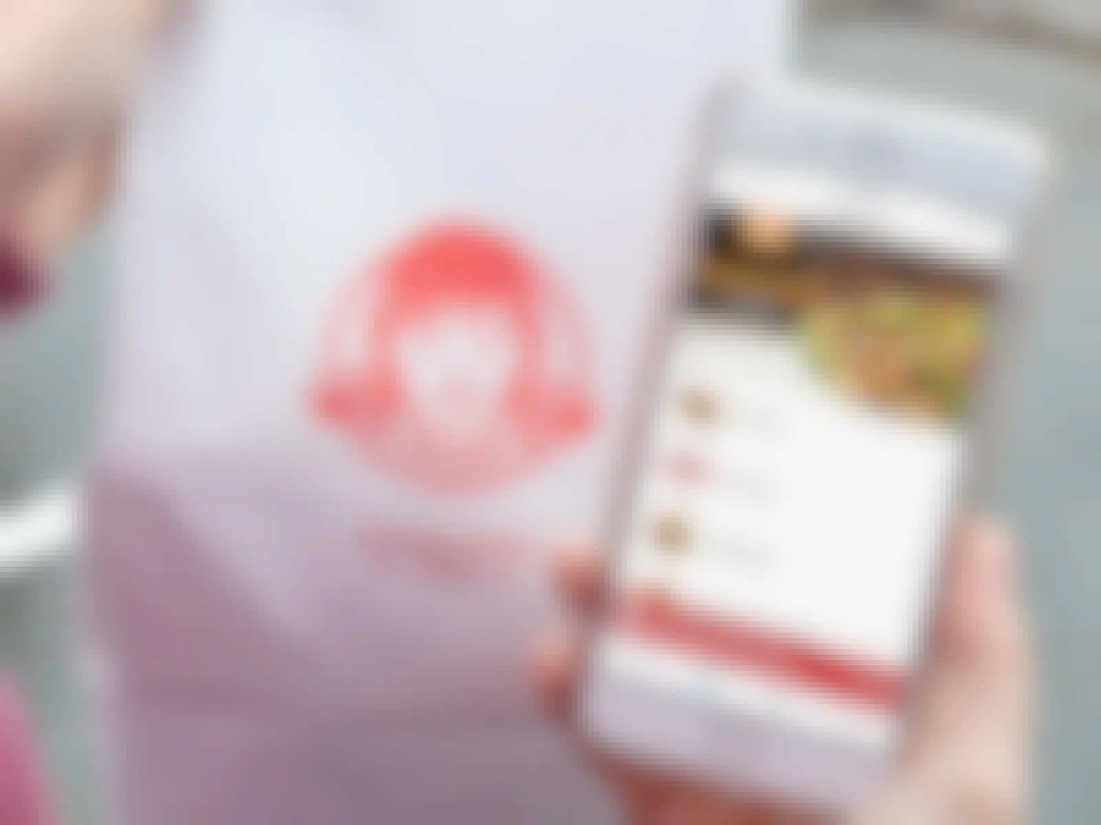 Someone holding a Wendy's takeout bag next to an iPhone displaying the Wendy's mobile app.