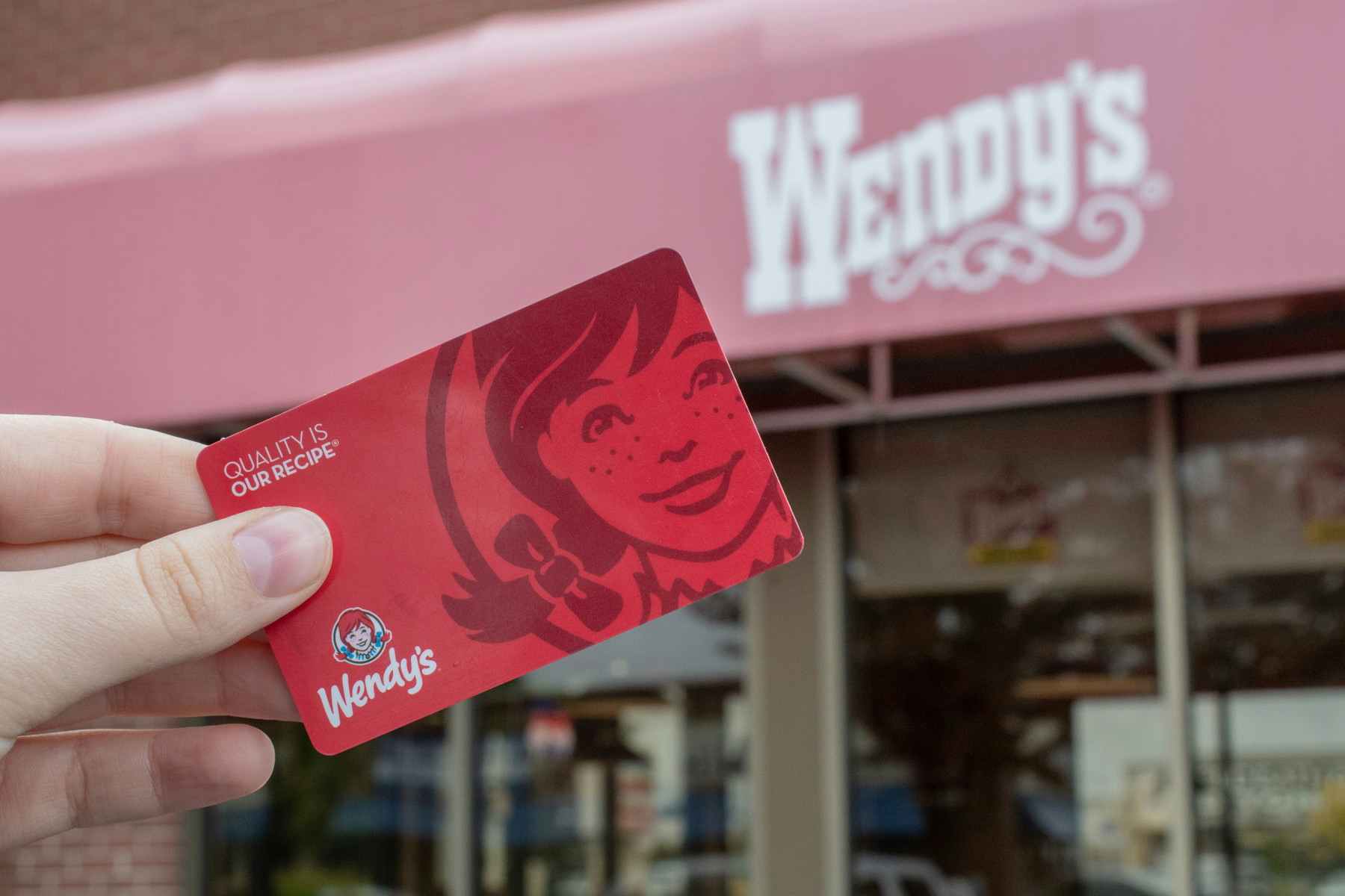 a wendys gift card being held in front of a wendys 