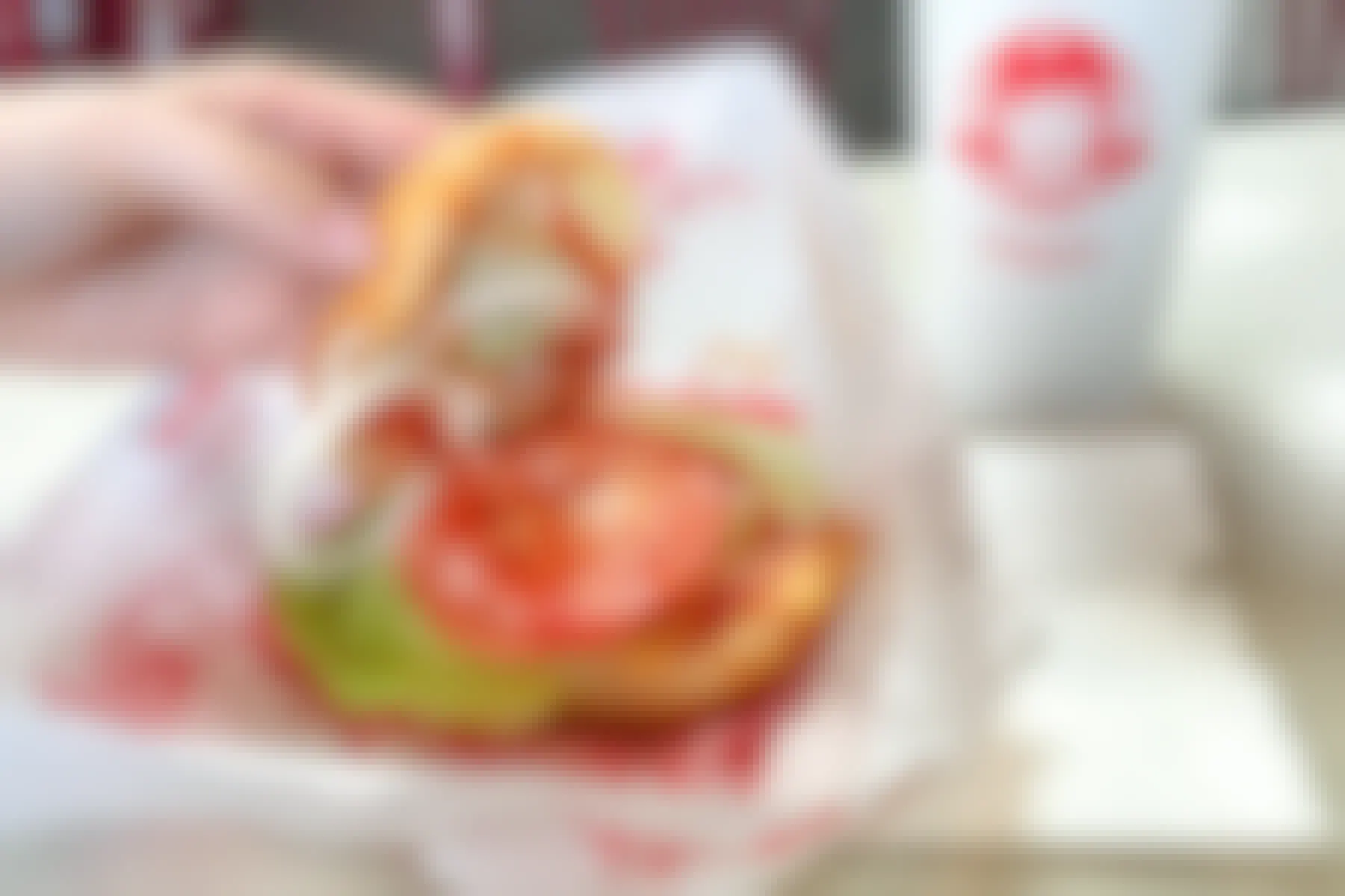A person's hand lifting the top bun off of a meatless Wendy's sandwich sitting on a paper wrapper next to a Wendy's drink cup.