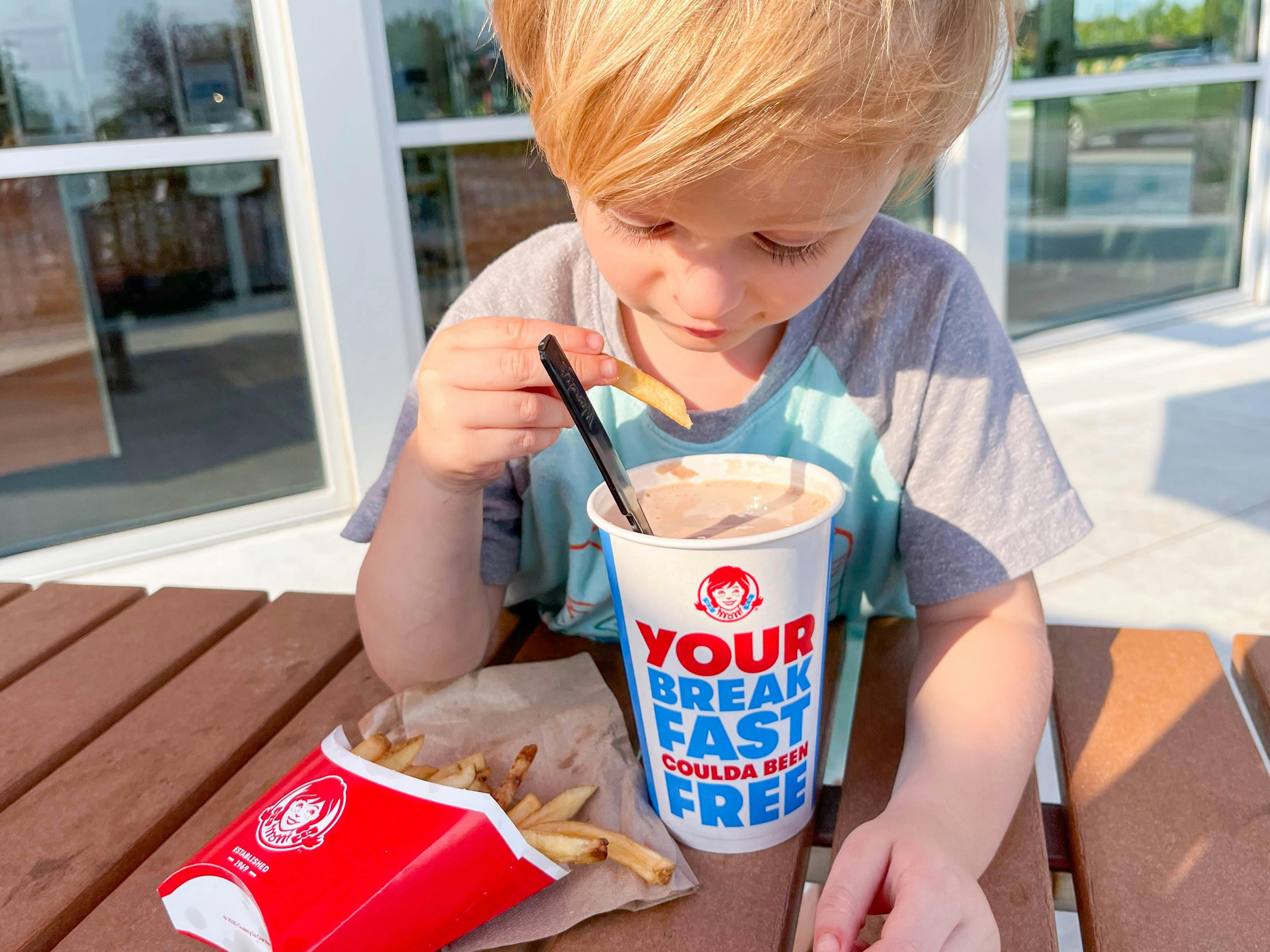 A kid dipping fry into a Wendy's frosty