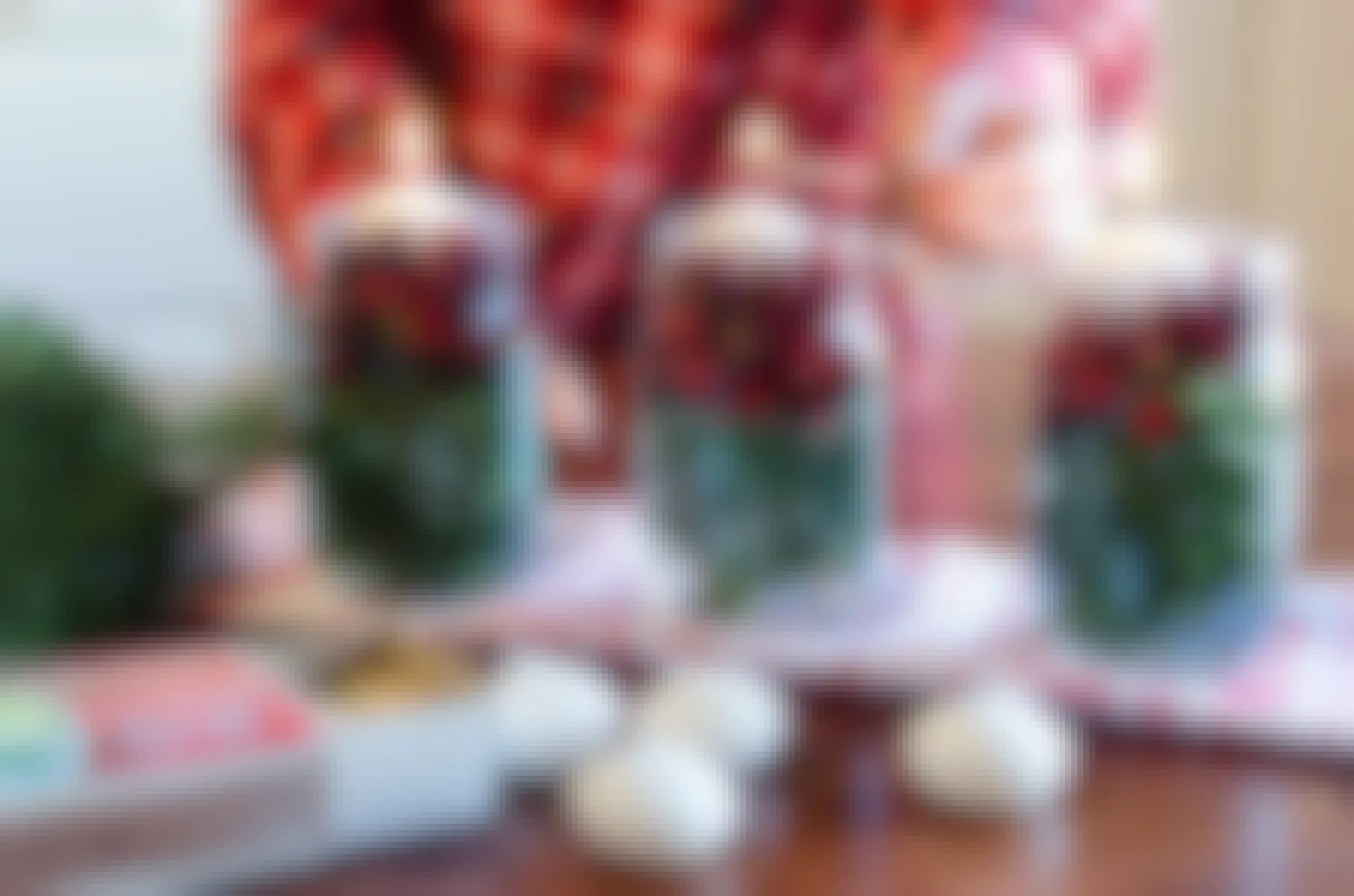 Floating candles being lit in mason jars filled with greenery and cranberries