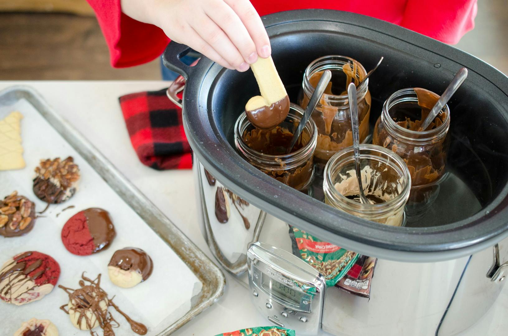 A person dipping a Christmas cookie in Chocolate. The chocolate is melted in a mason jar, kept warm with a crock pot.