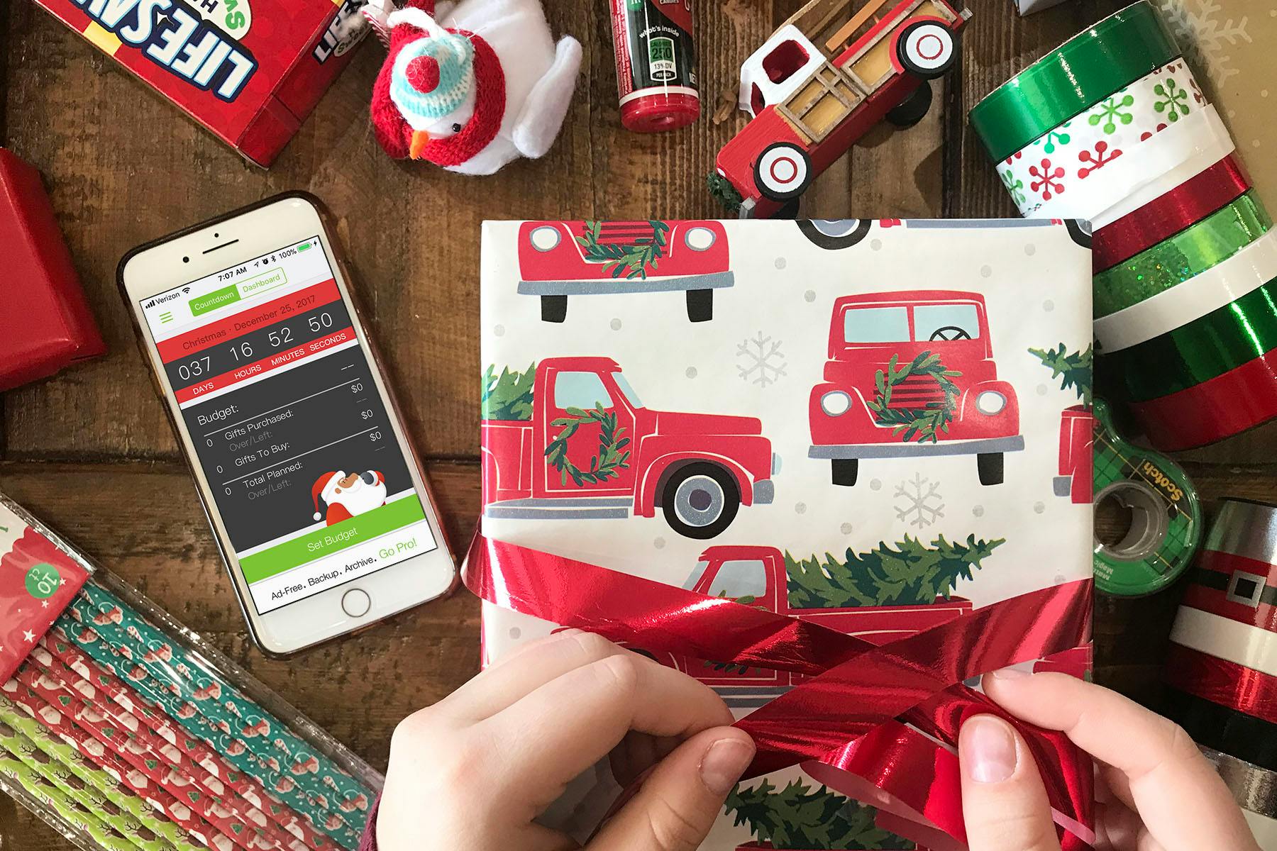 A gift being wrapped with a cell phone beside it displaying the Santas's bag gift tracking app.