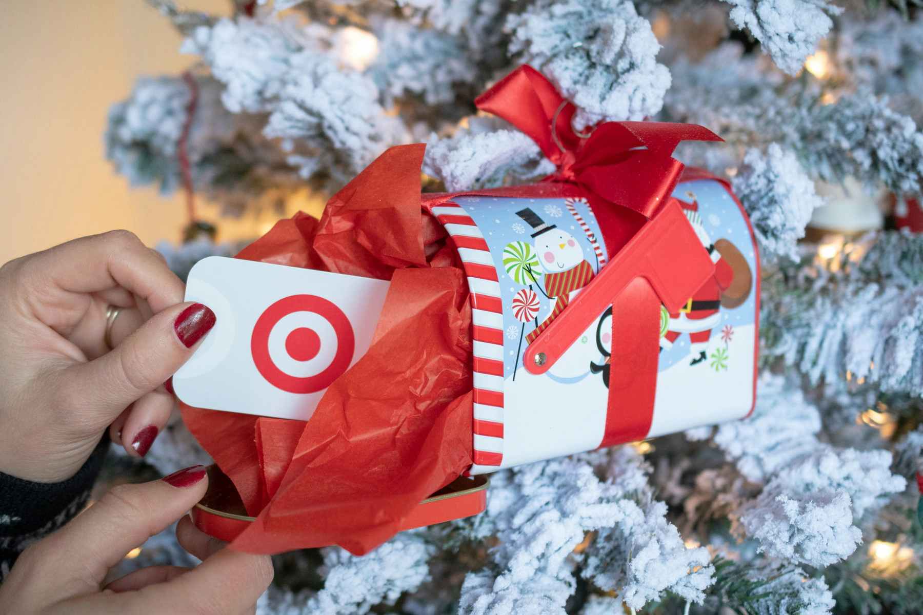 A person pulling a gift card from a Christmas tin, attached to the front of a Christmas tree.