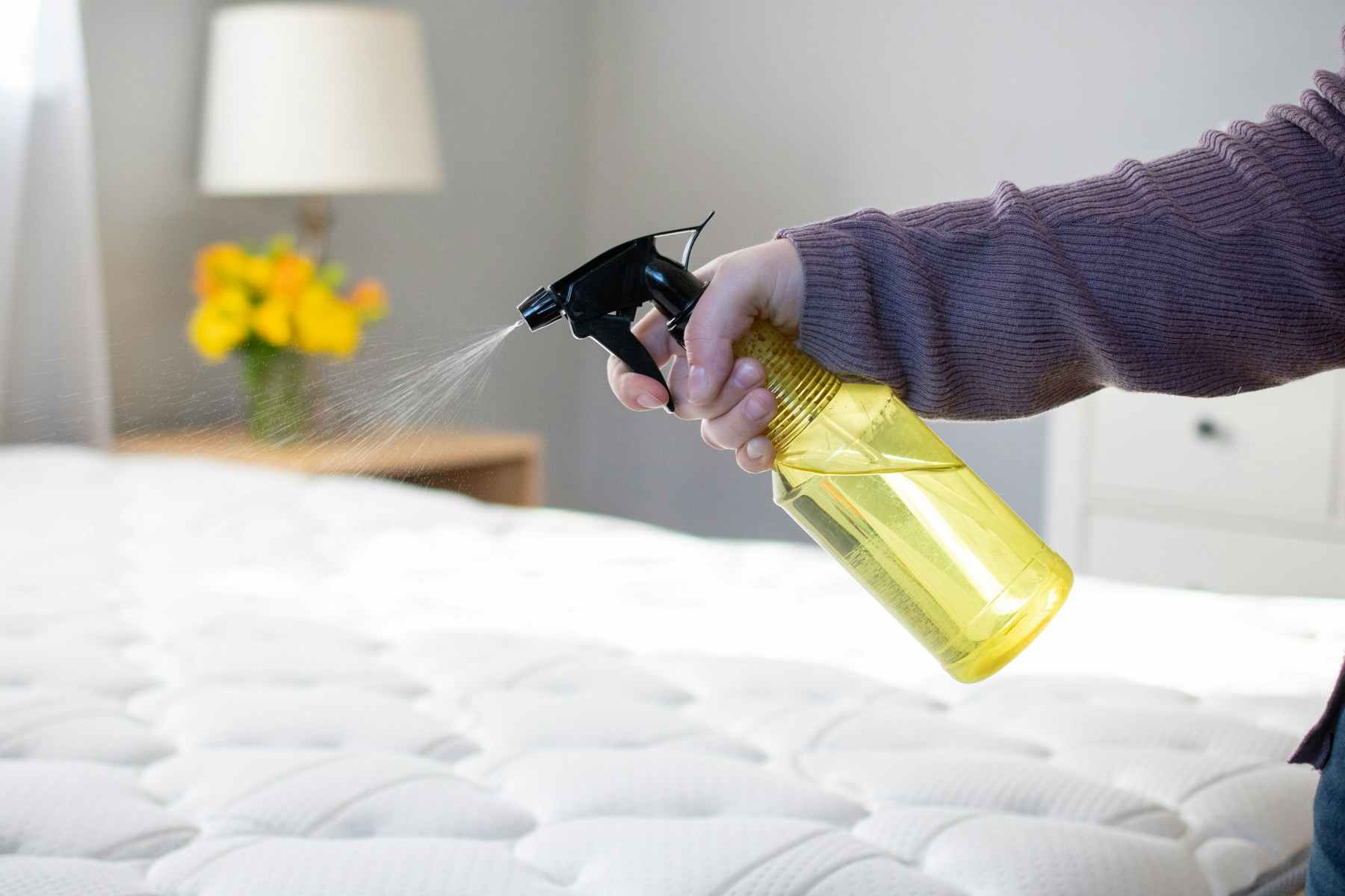 person using spray bottle to spray mattress with cleaning solution