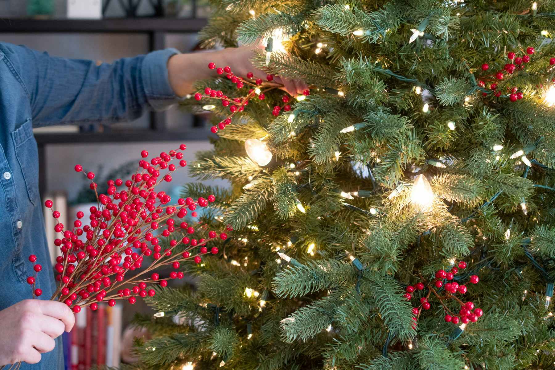 someone putting berries in a lighted christmas tree