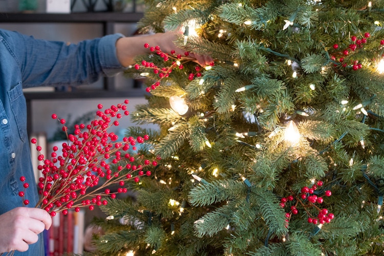 Red berry floral picks being put into a Christmas tree.