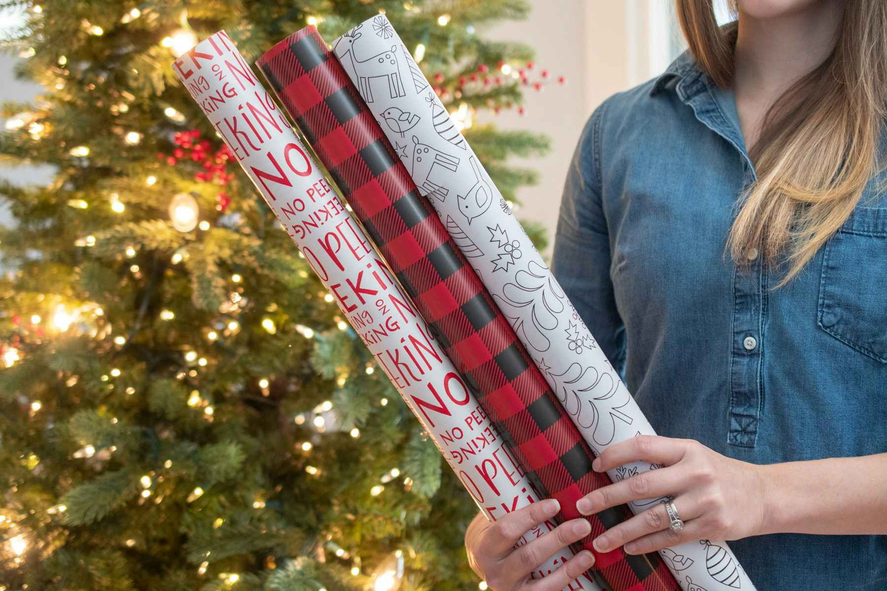 A person holding up three rolls of wrapping paper in front of a Christmas tree