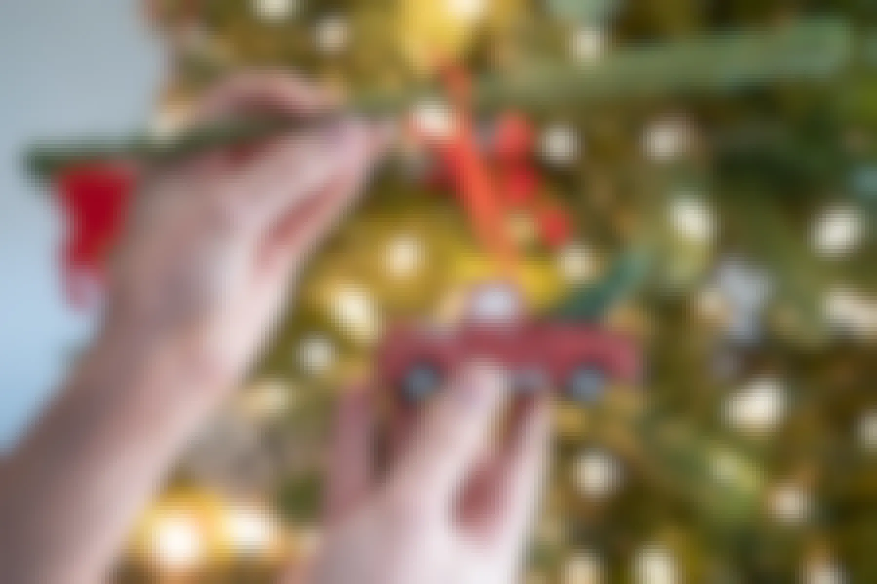 A person using an evergreen pipe cleaner to hang a heavy ornaments on a Christmas tree