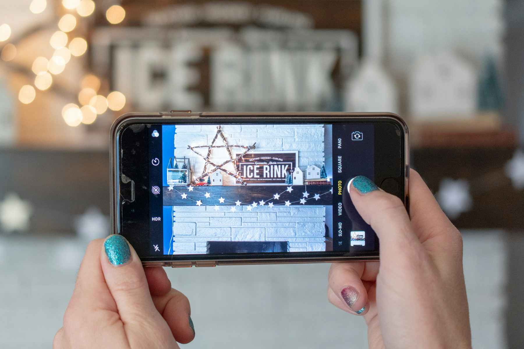 A person using a cell phone to take a photo fo a Christmas fireplace mantel. 