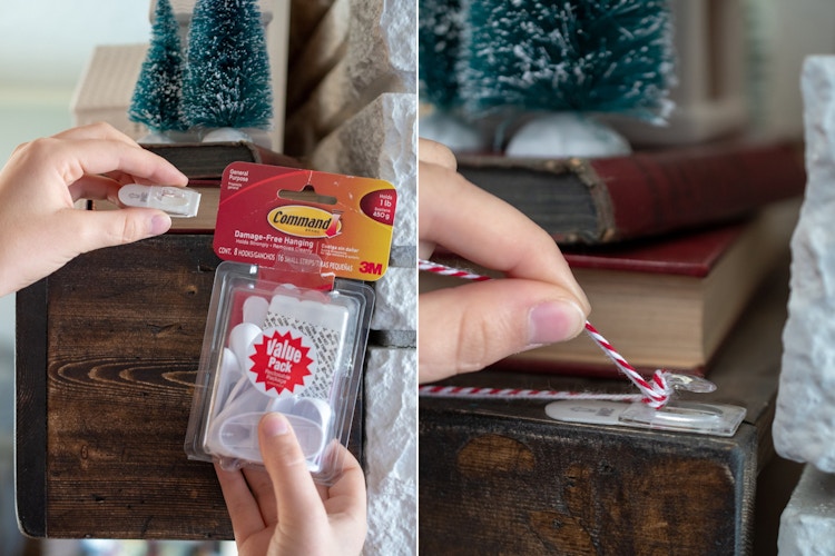 A person using a command hook to tie a garland onto a fireplace mantel. 