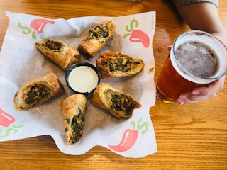 A basket with Chili's southwest egg rolls sitting next to a glass of beer on a table at Chili's.