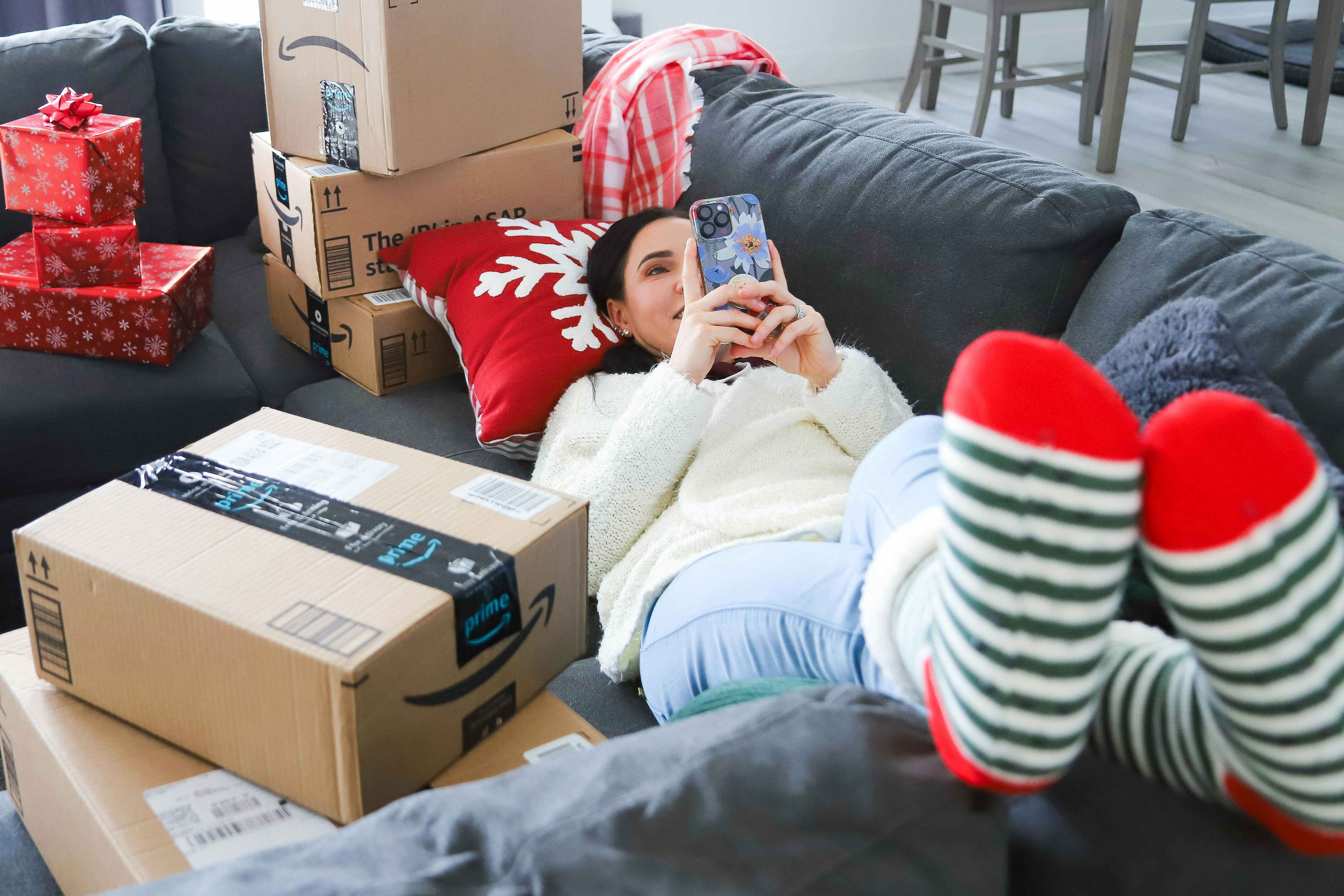 a woman looking at her phone while laying on couch near boxes 