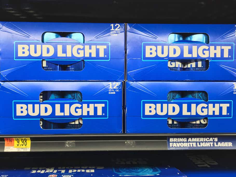 Four 12-pack boxes of Bud Light stocked on a cooler shelf in a grocery store.